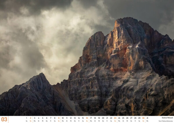 2025 Dolomiten Calendar, March. Photograph of Sextener Rotward, a red-faced mountain in dramatic light.