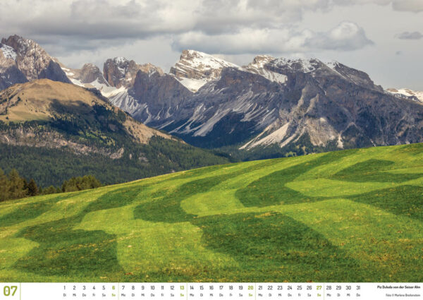 2025 Dolomiten Calendar, July. Photograph of snow-capped mountains beyond a mown meadow.