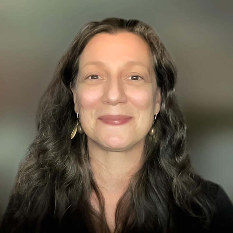 Head shot of Marlene Breitenstein, smiling, with long hair and a blurry background.